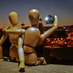 Two wooden mannequins taking a selfie overlooking a city.